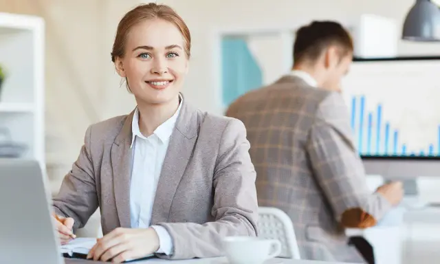 Mujer sonríe mientras se prepara para una entrevista de trabajo, tomando notas en su portátil.