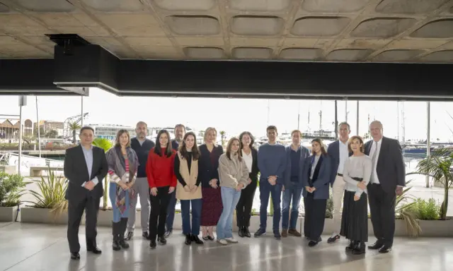 Grupo diverso posa para foto de graduación de un **advanced management program** frente a un puerto deportivo.