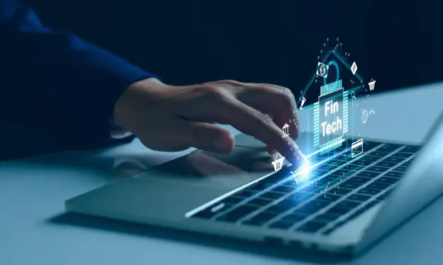 Dedo sobre teclado de laptop interactuando con un chip digital que muestra "Fin Tech" y varios iconos financieros, simbolizando el desarrollo de software fintech.