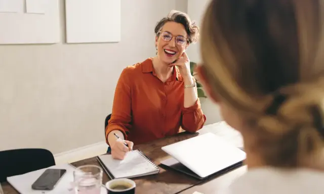 Mujer sonriente con gafas, tomando notas, discutiendo qué podrias aportar a la empresa.
