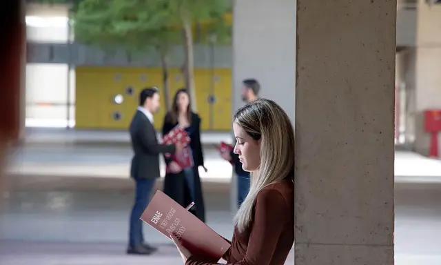 Estudiantes revisan materiales de estudio, como ejemplos de trabajos de oficina, en un campus universitario.