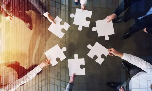 Manos unidas colocando piezas de rompecabezas, un símbolo de inteligencia colaborativa y trabajo en equipo para lograr un objetivo común.