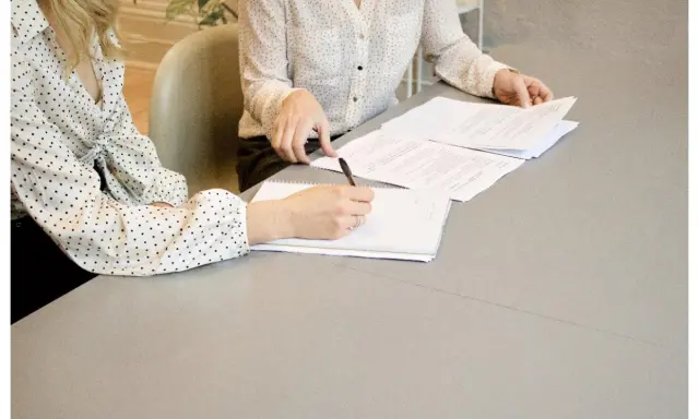 Dos mujeres revisan documentos en una mesa. Una escribe notas, un paso clave en cómo ser un CEO.