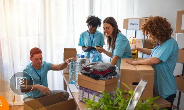 Voluntarios organizan donaciones. Un hombre revisa una lista, mientras otros empaquetan ropa y agua. Su cv volunteering es valioso.
