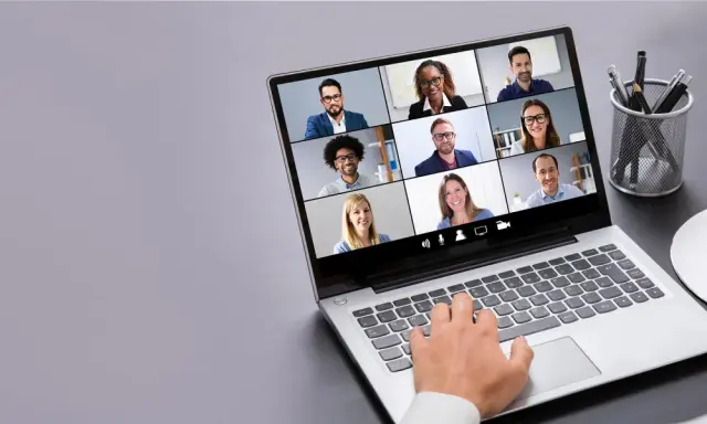 Persona interactúa con tecnología de videoconferencia, mostrando una cuadrícula de participantes en una reunión virtual.
