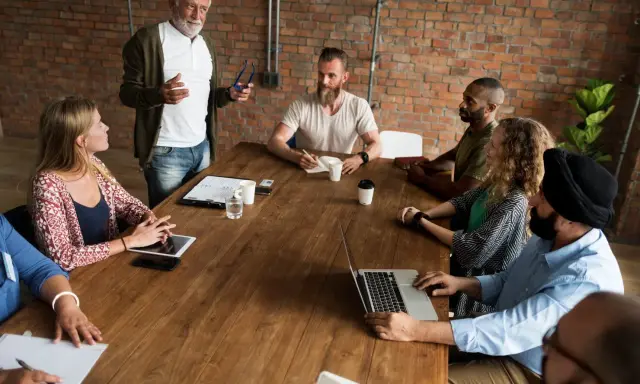 Un grupo diverso de personas participa en reuniones de empresa, discutiendo ideas alrededor de una mesa de madera.