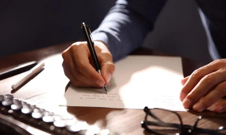 Mano escribiendo una carta formal con bolígrafo.