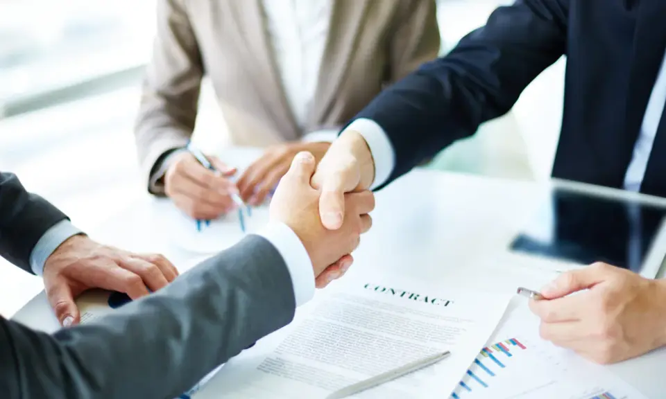 Apertón de manos entre hombres de negocios, con un contrato y gráficos sobre la mesa. Tácticas de negociación exitosas.