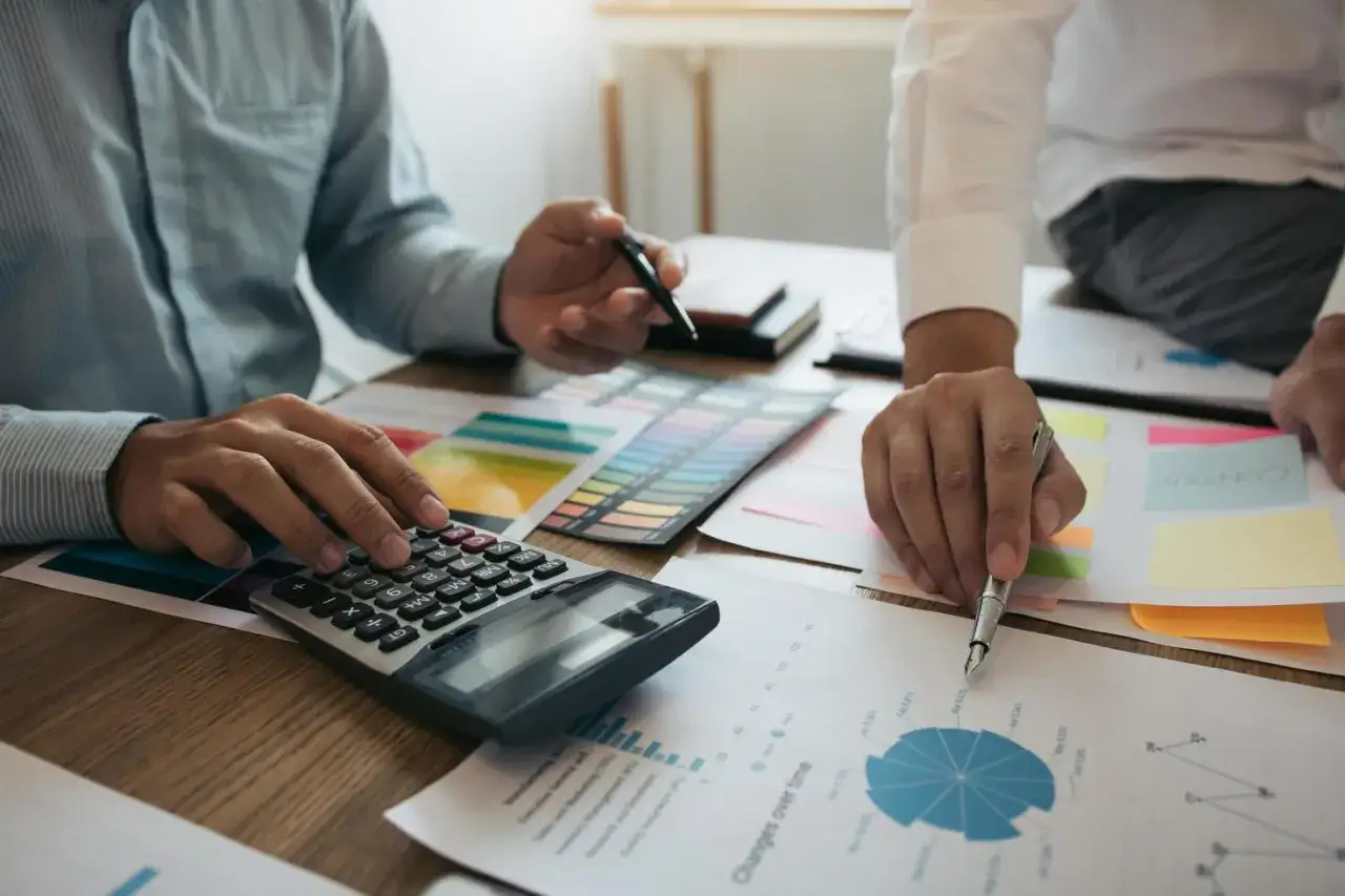 Dos personas analizan gr&aacute;ficos y usan una calculadora, mostrando c&oacute;mo comportarse en el trabajo con profesionalismo y atenci&oacute;n al detalle.