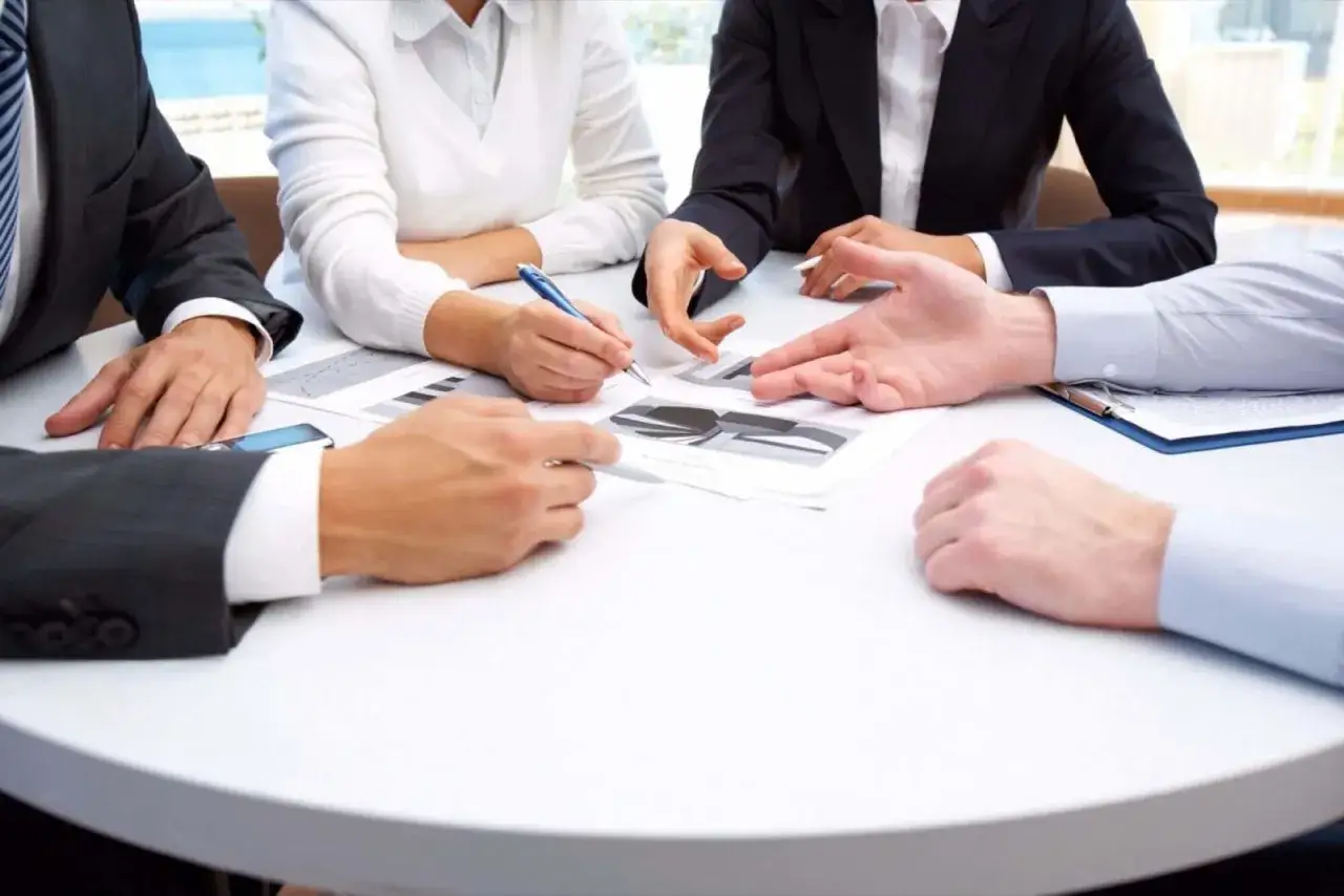 Manos discutiendo gr&aacute;ficos en una mesa blanca. Parece que estas reuniones largas apenas est&aacute;n comenzando.