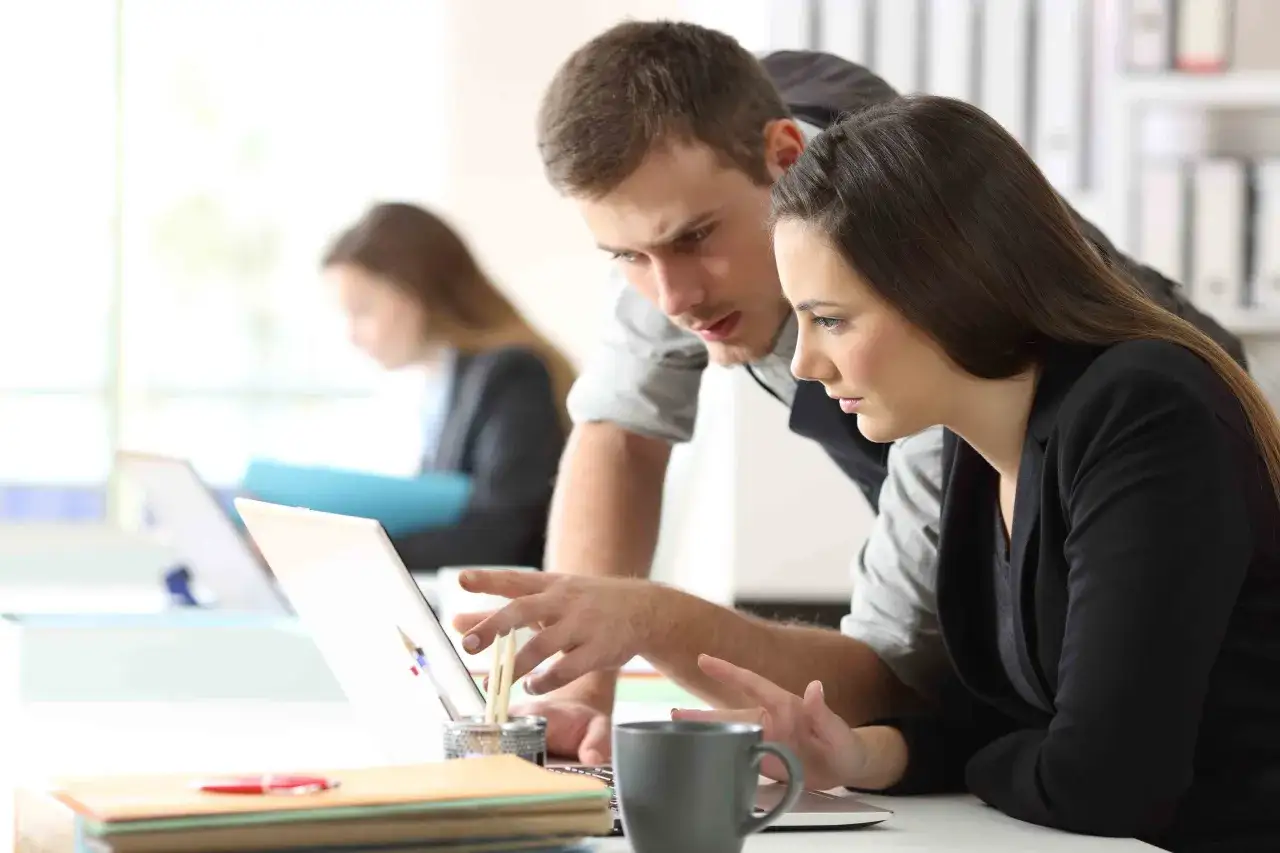 Dos colegas analizan un proyecto en una laptop, discutiendo lo que significa practicas no laborales.