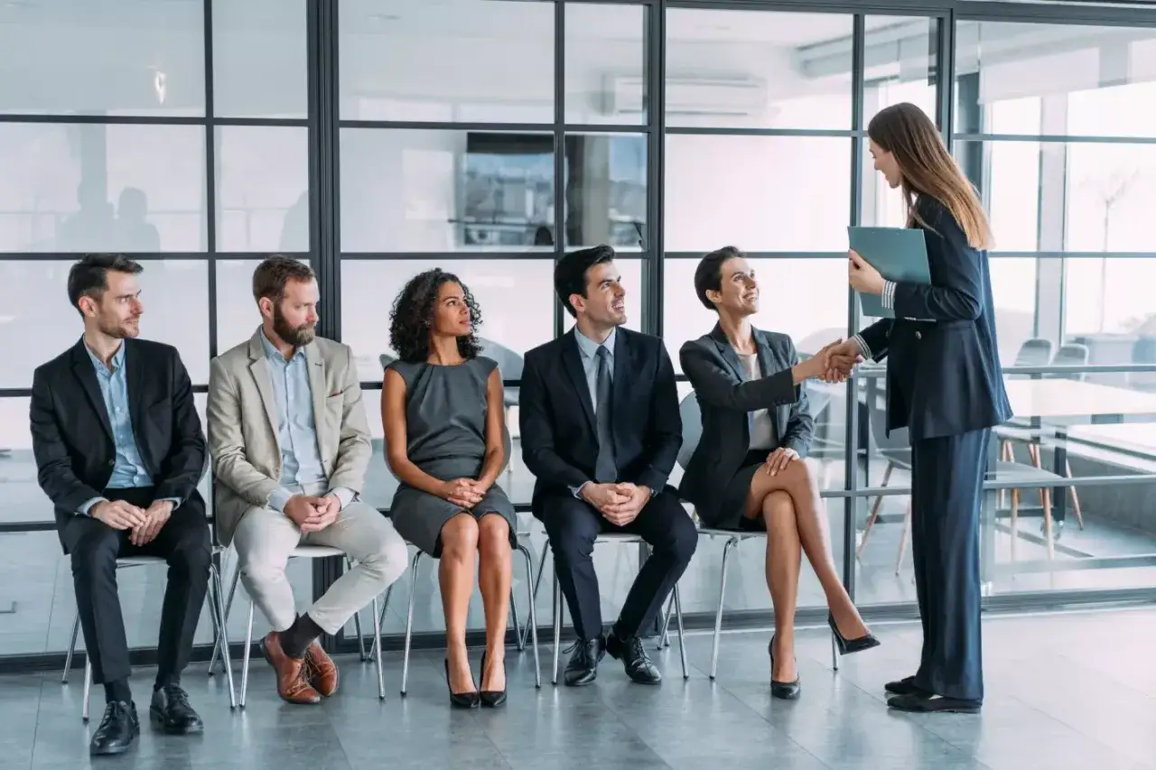 Candidatos esperan su turno para una entrevista de trabajo. Una mujer sonr&iacute;e mientras estrecha la mano de otra.