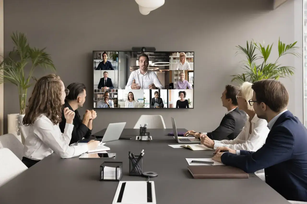 Equipo en reuni&oacute;n virtual. La pantalla muestra a varios colegas en una videollamada, facilitando la comunicaci&oacute;n y el chat interno de la empresa.