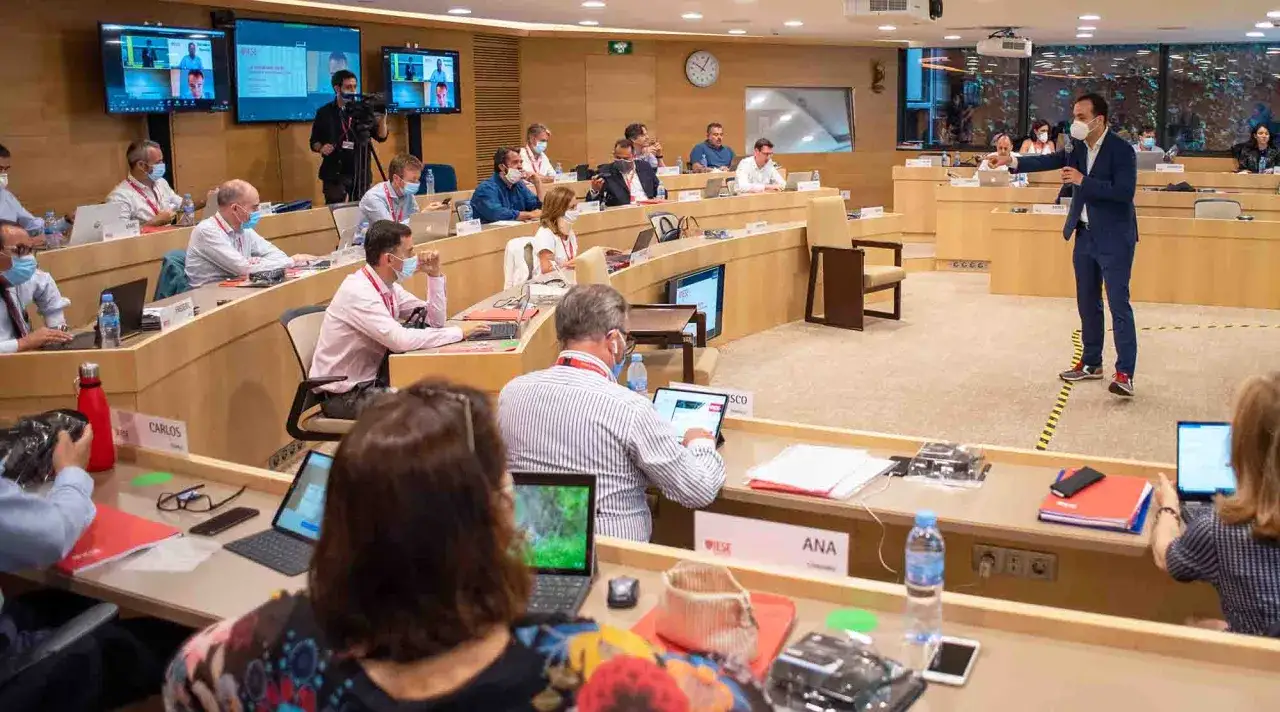 Un hombre da una charla en un auditorio. Los asistentes, con mascarillas, toman notas en sus portátiles. Esto es lo que se aprende en un MBA.