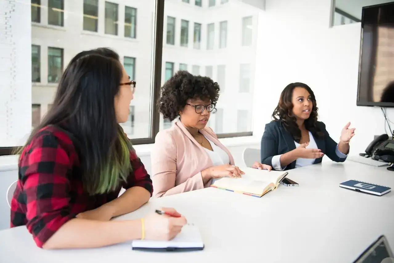 Tres mujeres en una reunión discuten ideas, cada una lista para aportar su perspectiva única.
