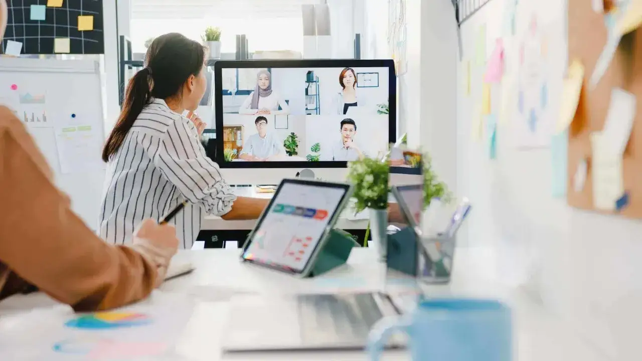 Mujeres colaborando en una reunión virtual. La pantalla muestra a varios miembros de equipos virtuales en una videollamada.