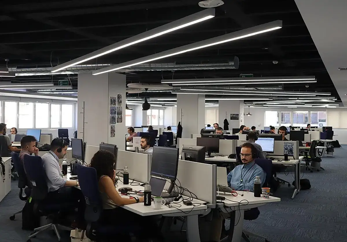 Oficina moderna con empleados trabajando en sus ordenadores. Un joven disfruta de su spain internship en este entorno colaborativo.