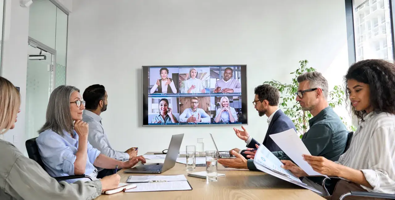Equipo en una reunión de pie, colaborando en un proyecto con colegas en pantalla.
