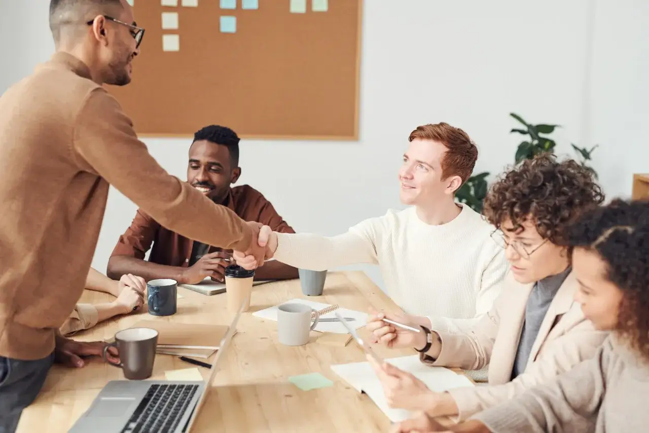 Equipo diverso en reunión, estrechando manos. Un buen ambiente para mejorar la comunicación interna de una empresa.