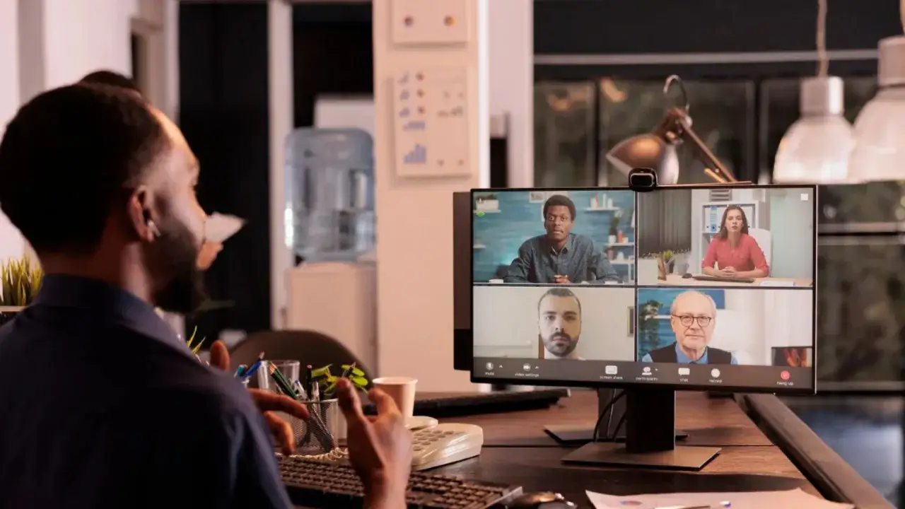 Un hombre participa en una videollamada con cuatro colegas, usando el chat para comunicaci&oacute;n instant&aacute;nea.