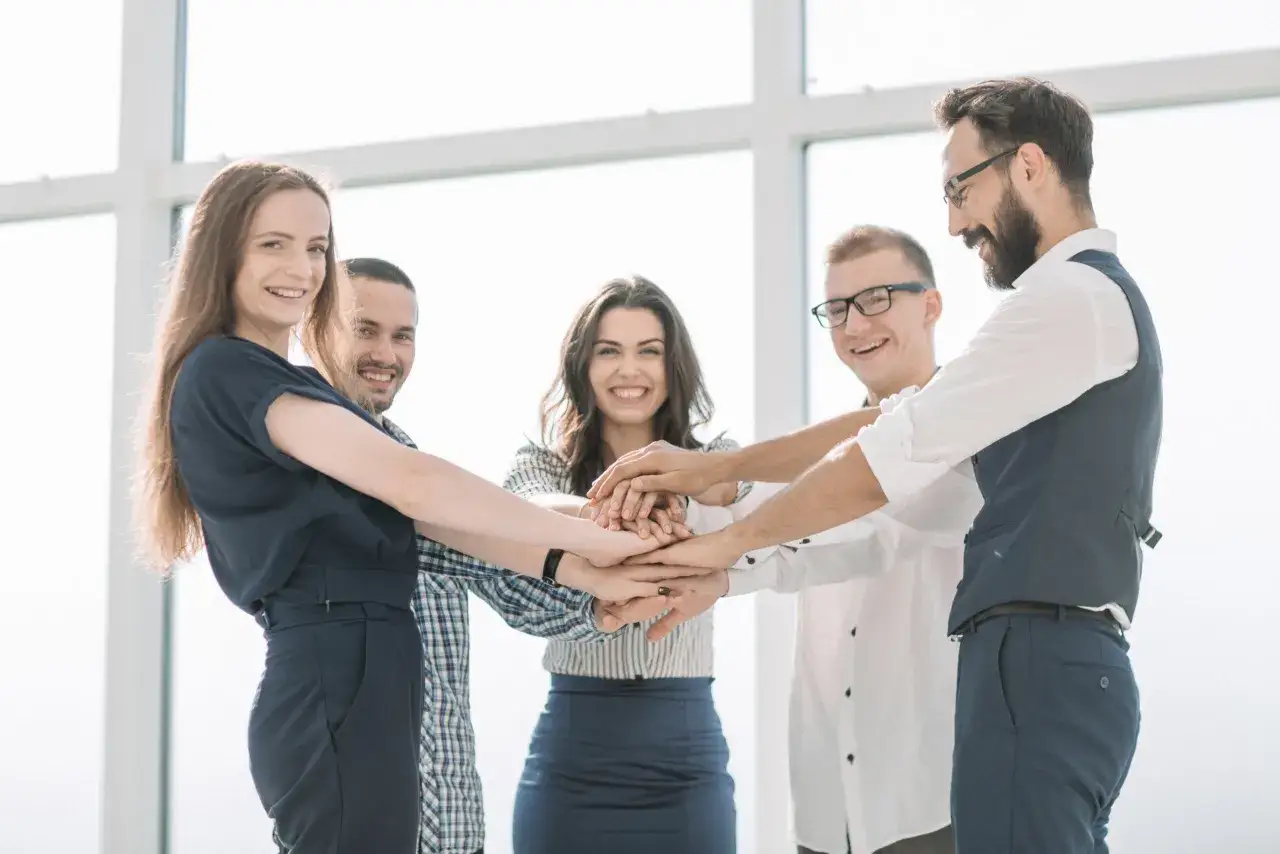 Equipo unido, reflejo de un liderazgo &eacute;tico. Cinco personas sonr&iacute;en mientras juntan sus manos en se&ntilde;al de compromiso y colaboraci&oacute;n.