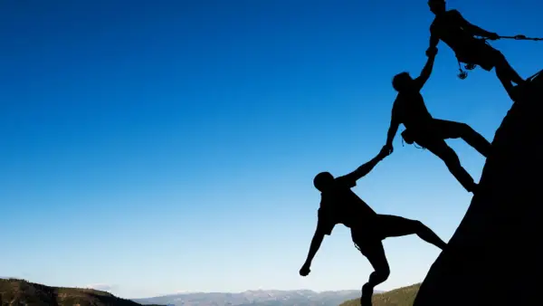 Siluetas de escaladores ayudándose mutuamente en una roca. Un ejemplo de cómo comportarse en el trabajo: colaboración y apoyo.